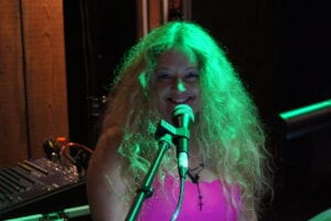 A woman with long hair is singing into a microphone.