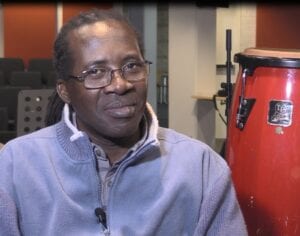 A man in glasses and a blue jacket is smiling.