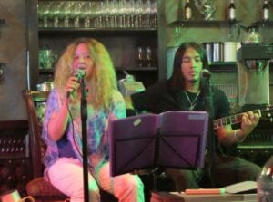 A woman holding a microphone and another man playing guitar.